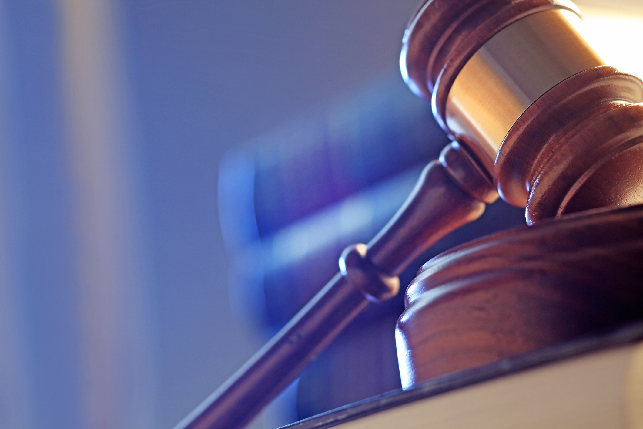 A close up of a gavel in front of a stack of law books photographed with a shallow depth of field and from a low camera angle.