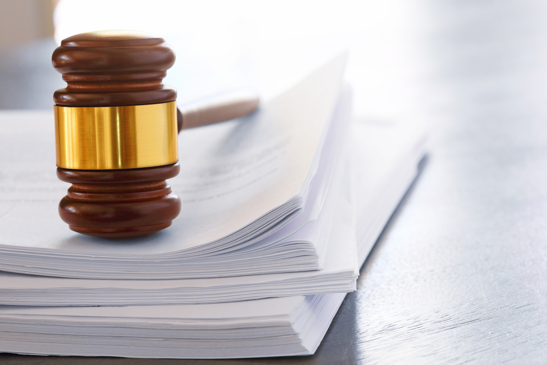 A gavel rests on top of a stack of legal documents. Photographed with a very shallow depth of field.